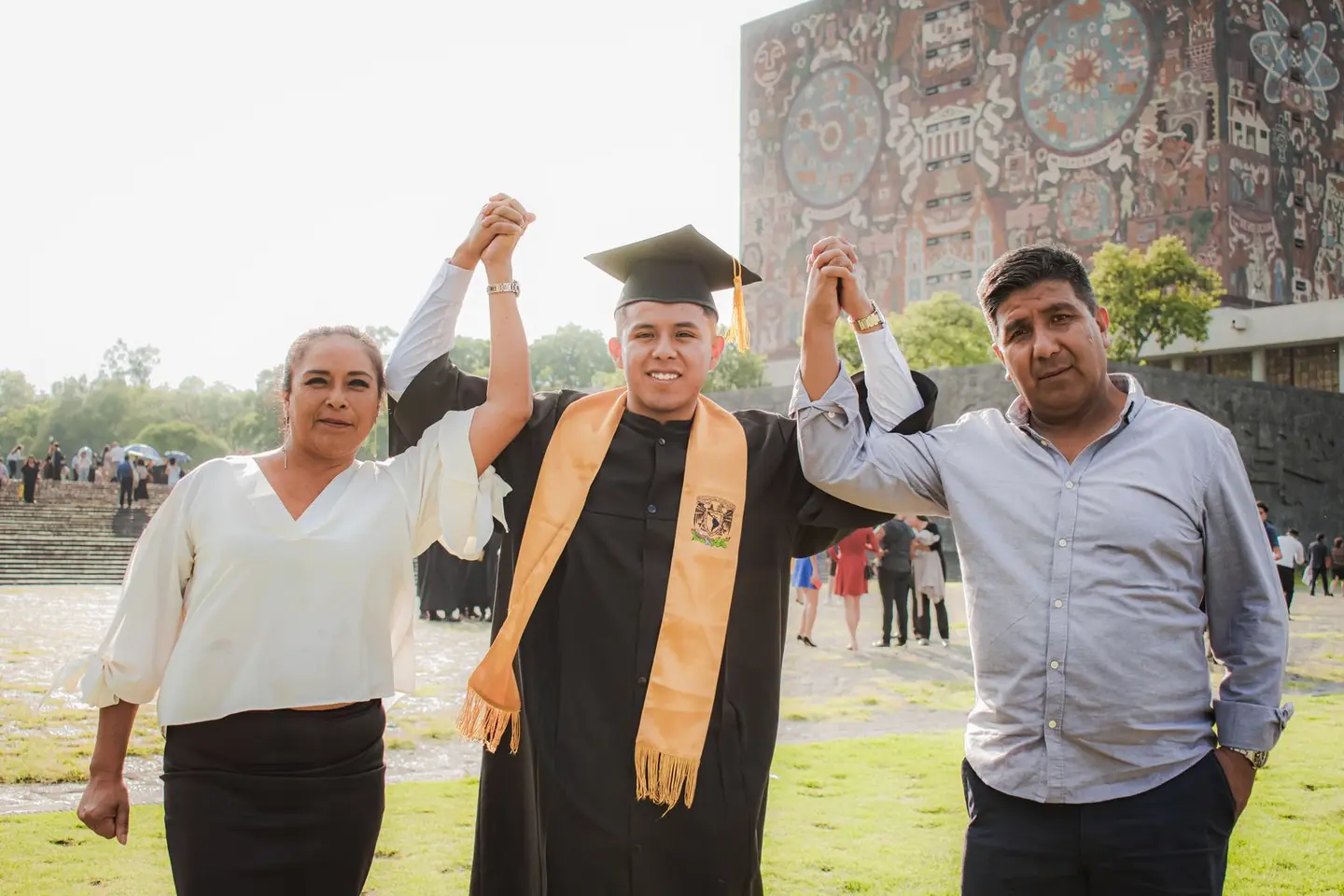 A university graduate in a cap and gown standing with his parents outdoors
