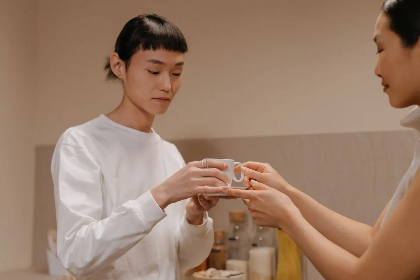 A mother passing a cup to her teenage daughter in their kitchen